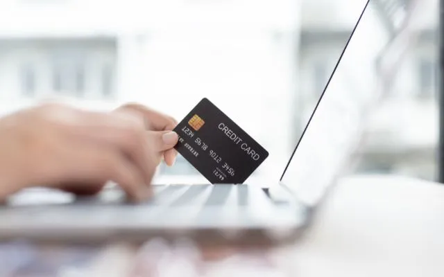A person holding a credit card in front of a laptop